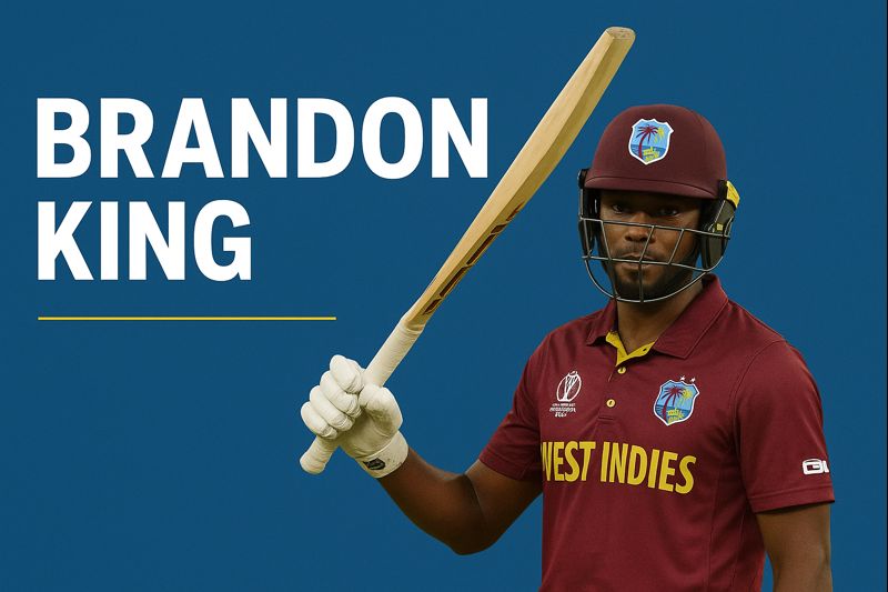 "West Indies cricketer Brandon King in maroon jersey holding a raised cricket bat against a blue background."